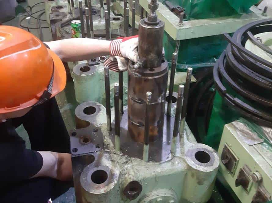 Marine engineer inspecting large engine part with tools and equipment.