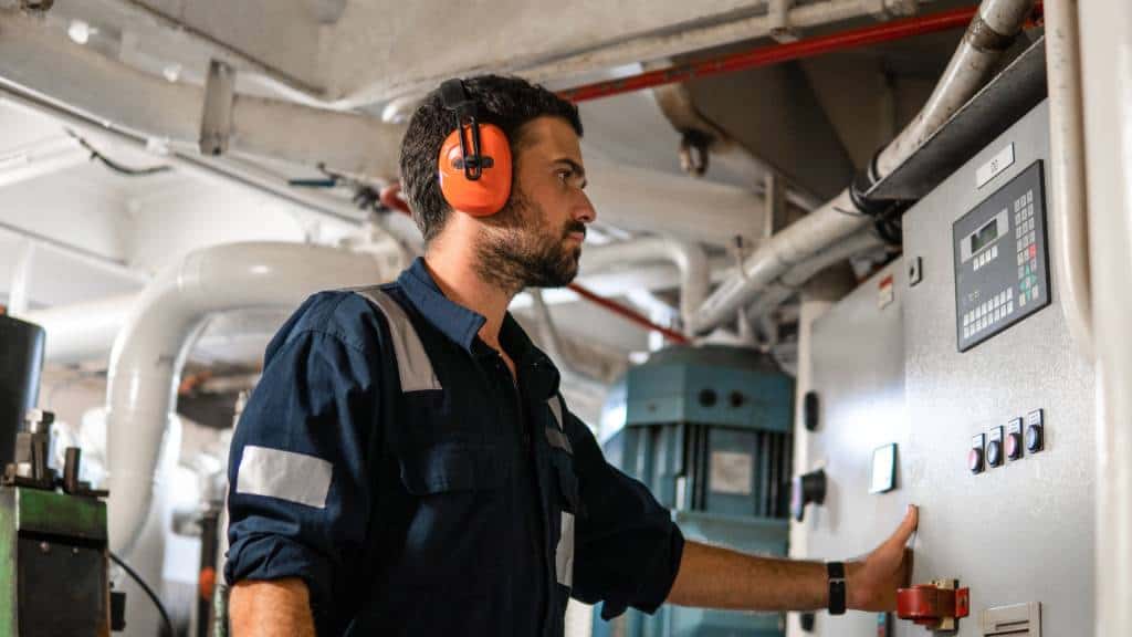 Marine engineer with headphones operating control panel on ship.