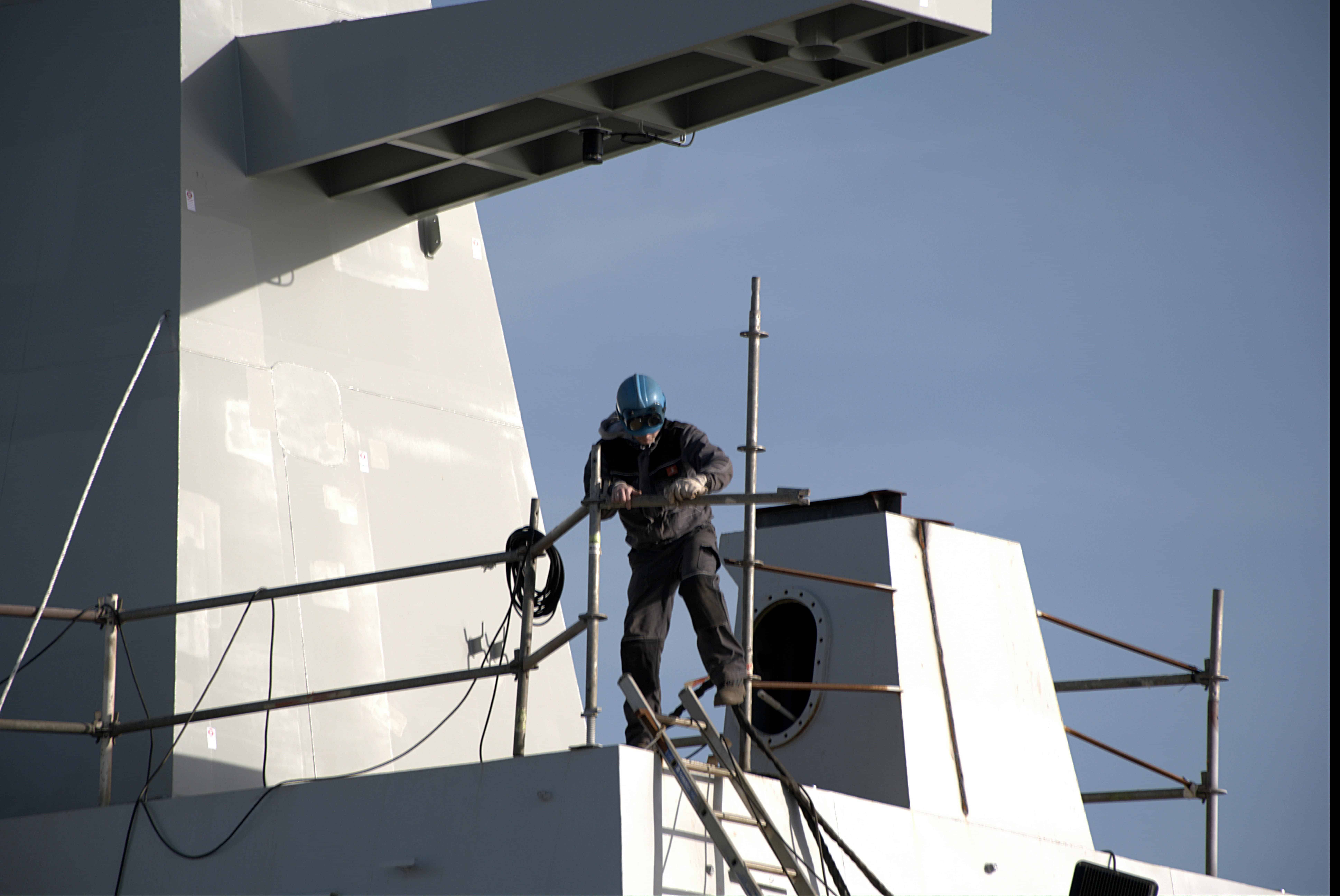 Marine engineer in safety gear working on ship's exterior.